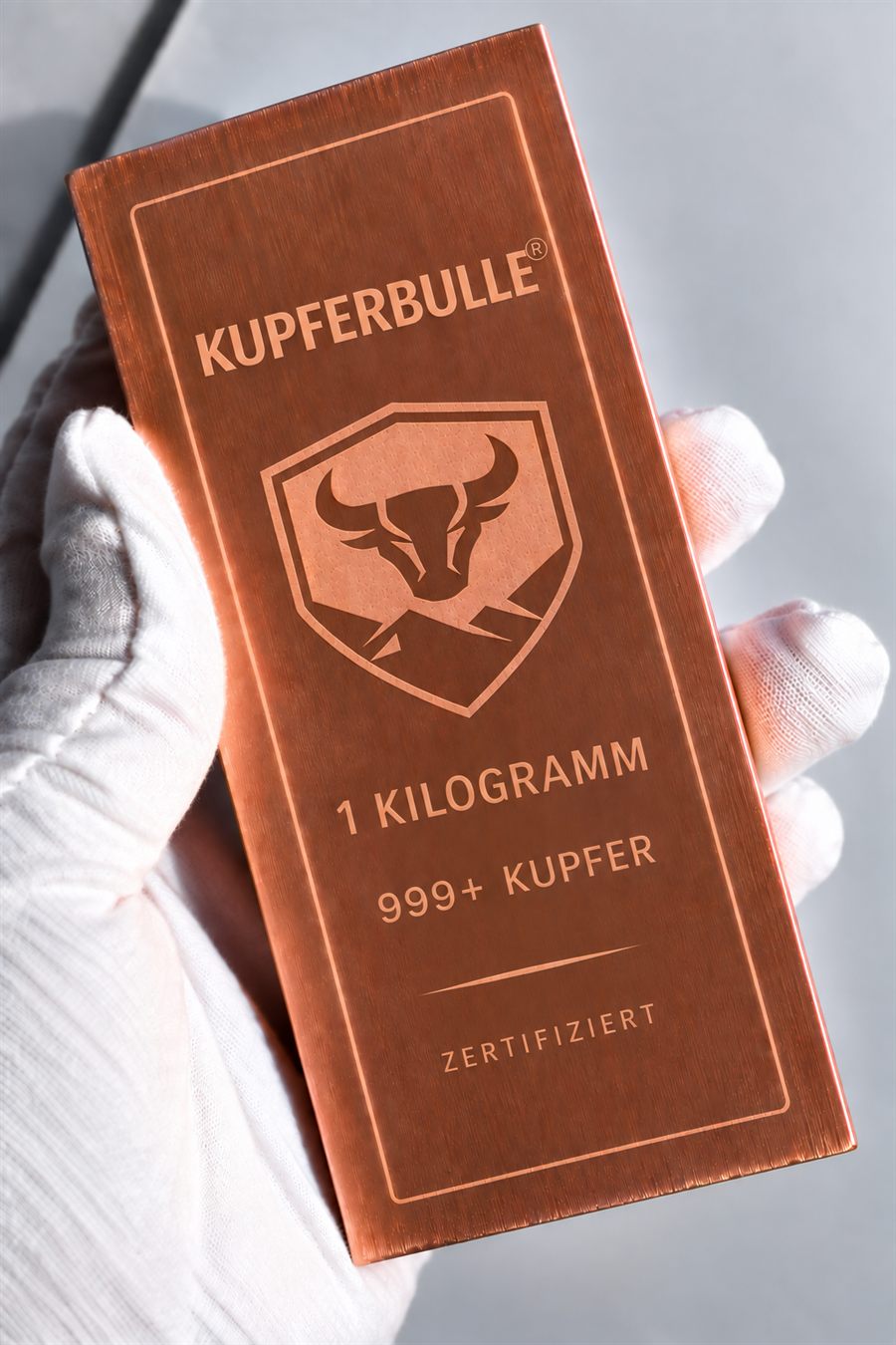 Kupferbulle-Barren, 1 Kilogramm 999er Kupfer, satiniert und lasergraviert, in einer Hand mit weißem Handschuh
